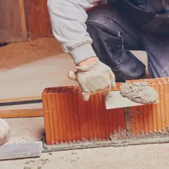 Murarz nakłada zaprawę na pustaki ceramiczne za pomocą kielni.