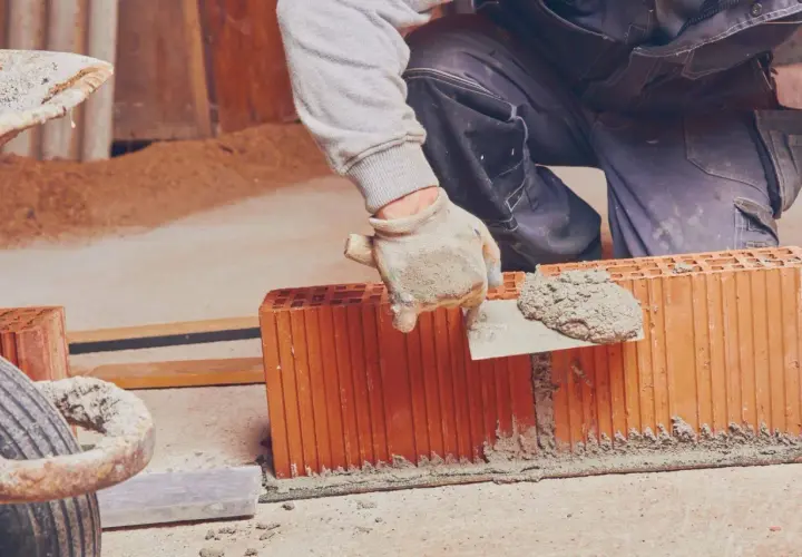 Murarz nakłada zaprawę na pustaki ceramiczne za pomocą kielni.