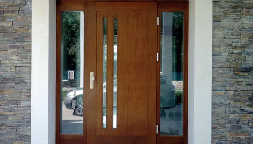 Brązowe drzwi wejściowe z przeszkleniami, obok kamiennej ściany.